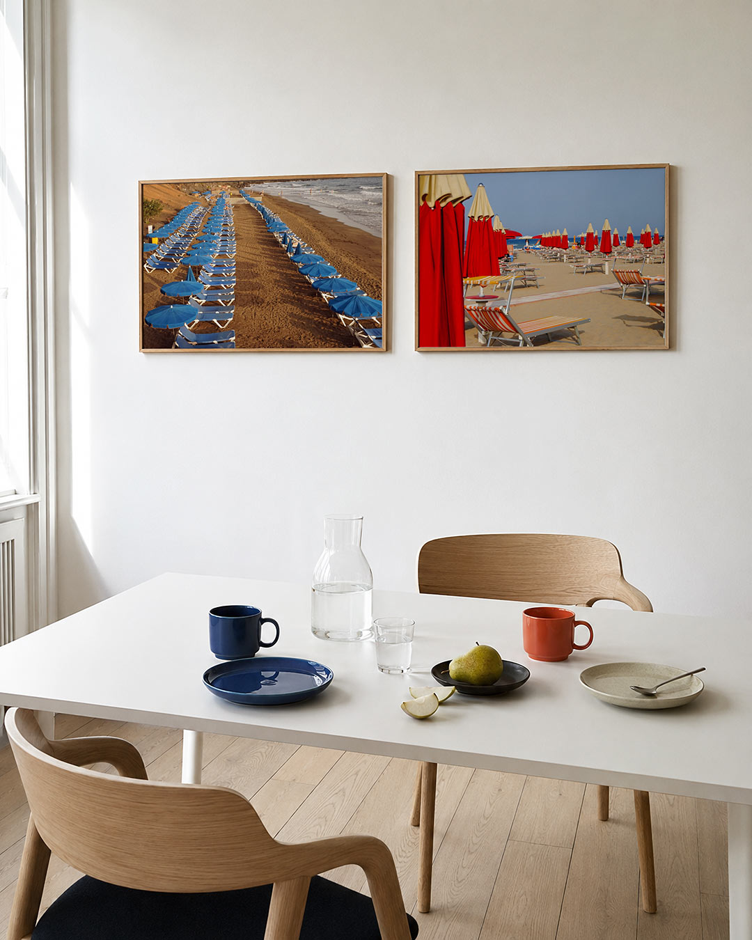 Tweedelige posterset met een ritmische ordening van blauwe parasols en ligbedden op een zandstrand, getoond in een interieur